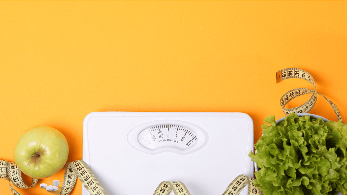 Bathroom scale with a measuring tape, a green apple and lettuce on an orange background