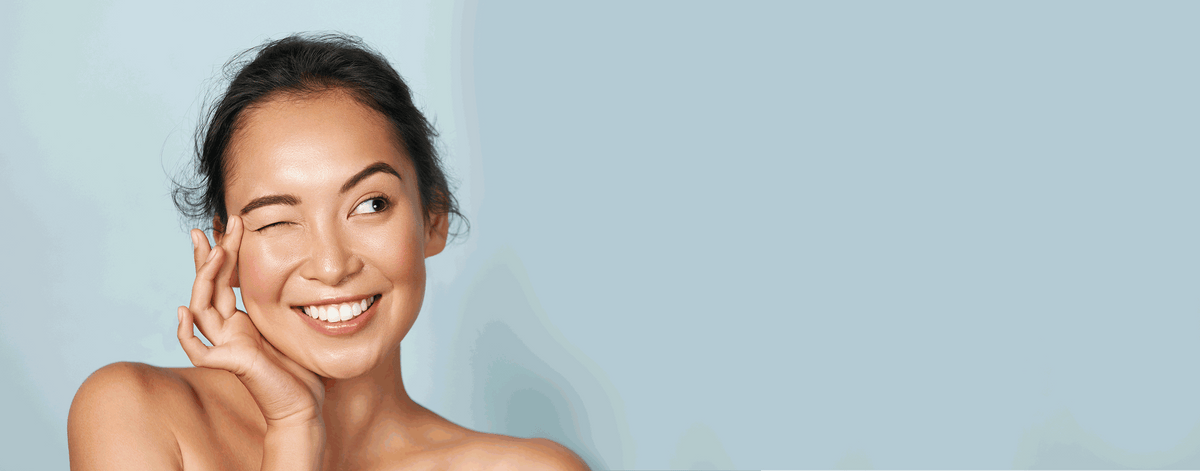 Smiling woman with glowing skin, winking against a pale blue background