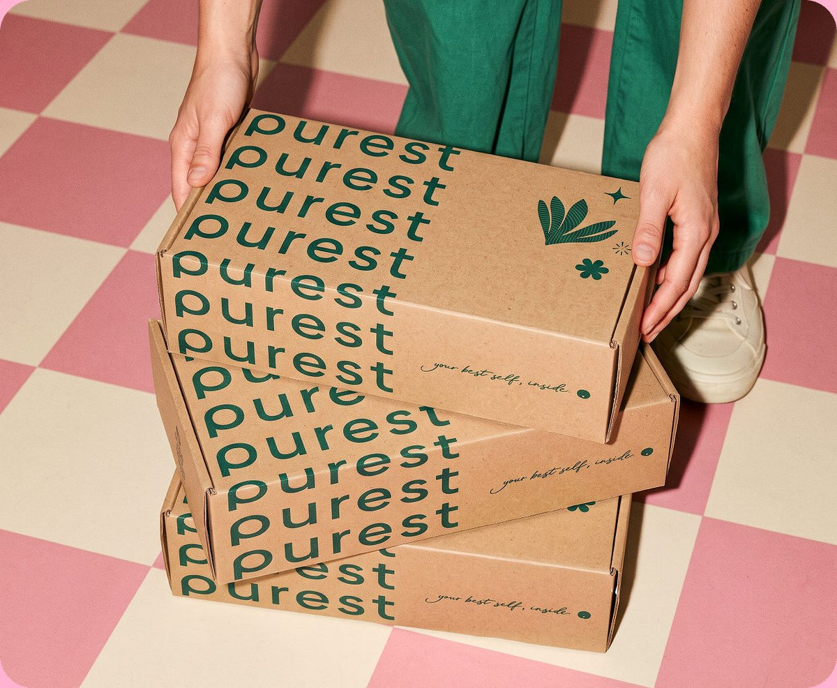 A shopper in green trousers stacking Purest delivery boxes on a pink and cream checked floor